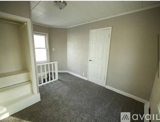 A room with a carpeted floor, a white door, and a window with white railings.
