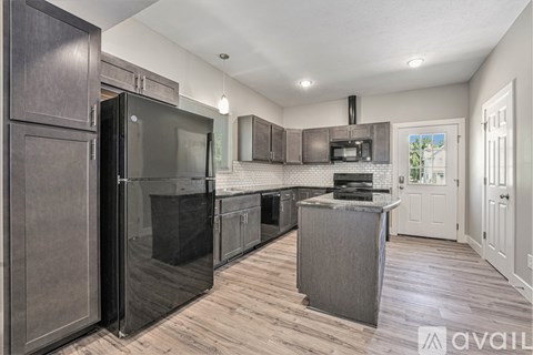 A kitchen with a black refrigerator and wooden floors.