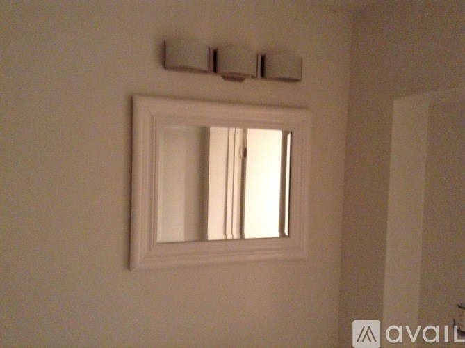 A white framed mirror is mounted on a wall above a light switch.
