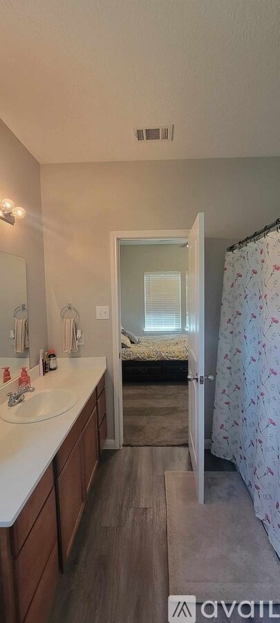 A bathroom with a sink, mirror, and a bedroom with a bed and a window.
