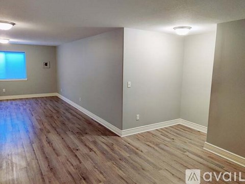 A room with wooden flooring and a window on the left side.