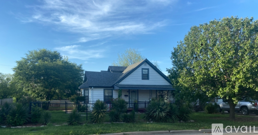 A house with a blue roof and white walls is surrounded by greenery.