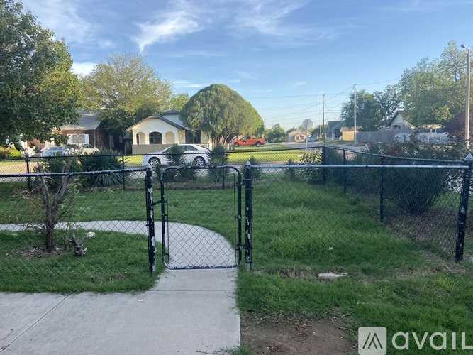 A black fence surrounds a green area with a pathway leading to a house.