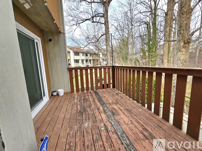 A wooden deck with a railing and a view of trees and buildings in the background.
