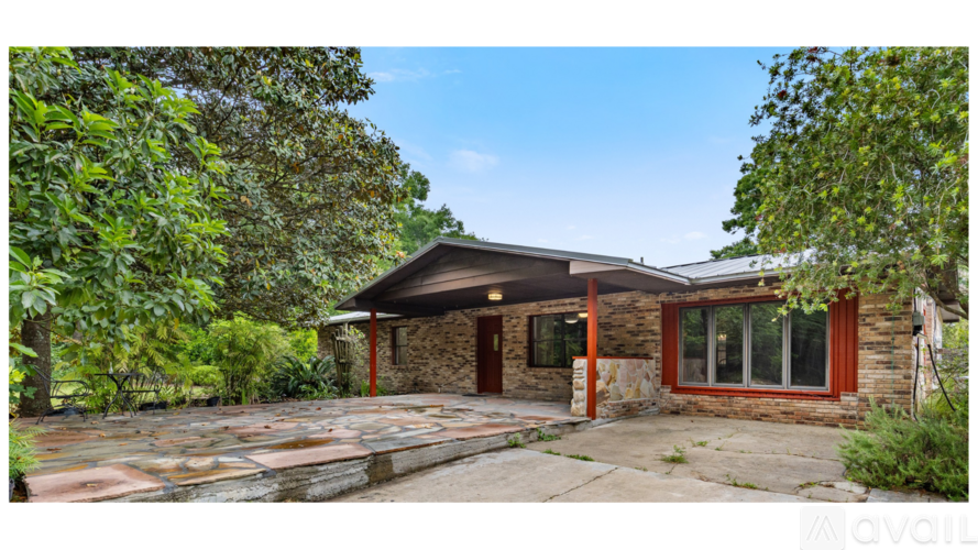 A house with a stone wall and a red door is surrounded by greenery.