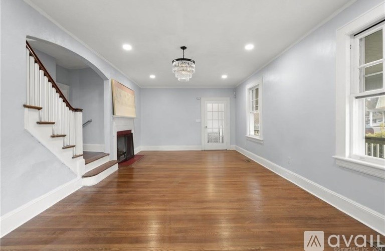 A spacious room with wooden floors and a staircase on the left side.