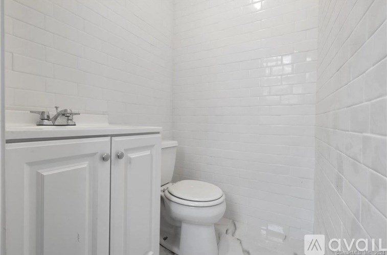 A white toilet sits next to a white sink in a white tiled bathroom.