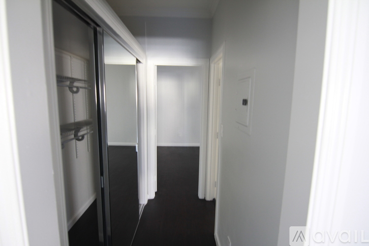A room with wooden floors and white walls, with a door on the left and a window with blinds on the right.