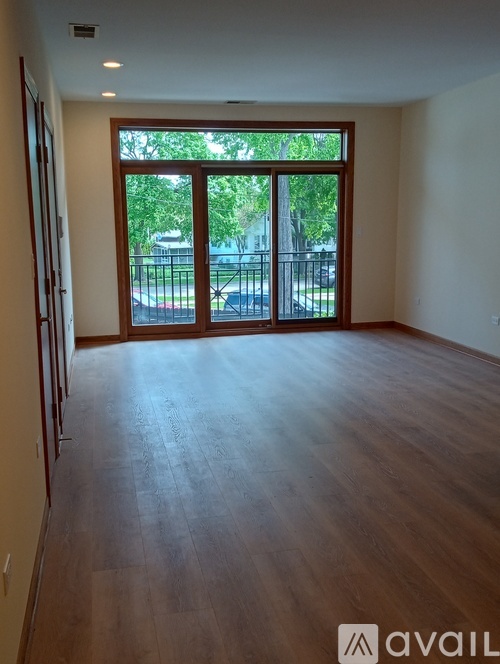 A room with wooden floors and a large window with a view of a parking lot.