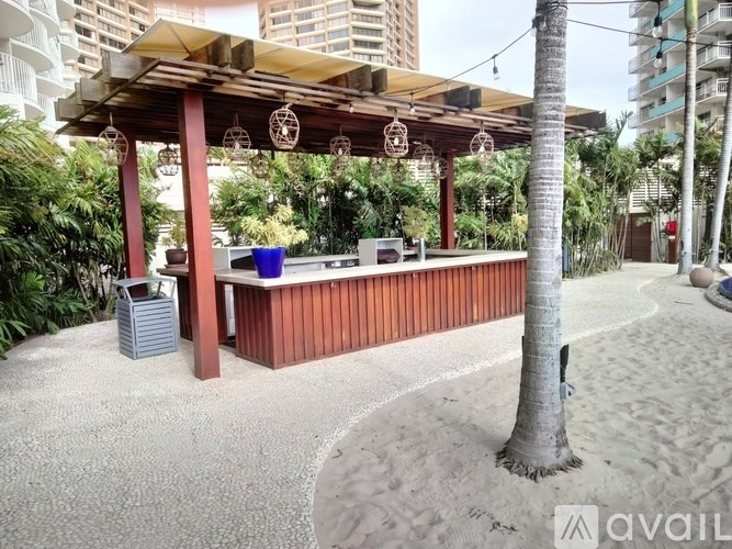 A wooden bar with a red roof is surrounded by sand and palm trees.
