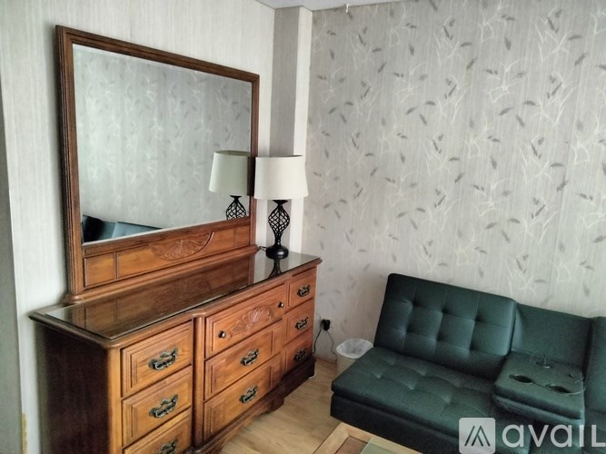 A green sofa sits in front of a wooden dresser with a mirror above it.