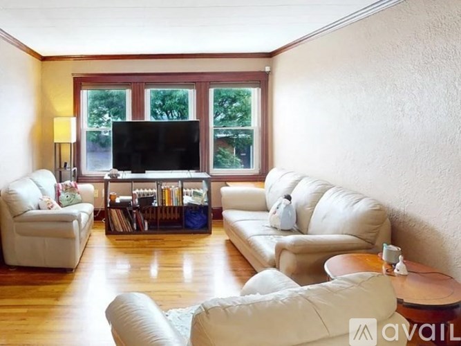 A living room with a white sofa, a white armchair, a white chair, a white ottoman, a white coffee table, a white side table, a white lamp, a white TV stand, a white bookshelf, and