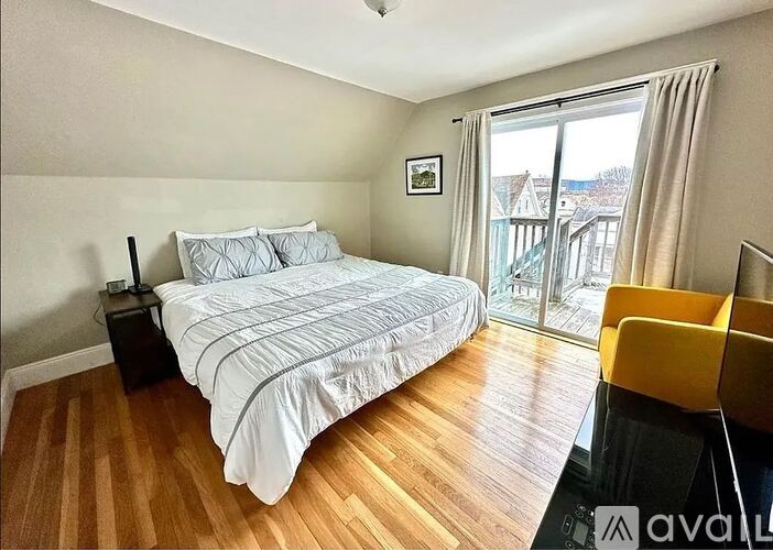 A bedroom with a large bed and a balcony with a view of buildings outside.