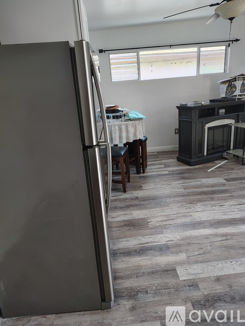 A room with a grey refrigerator and a wooden floor.