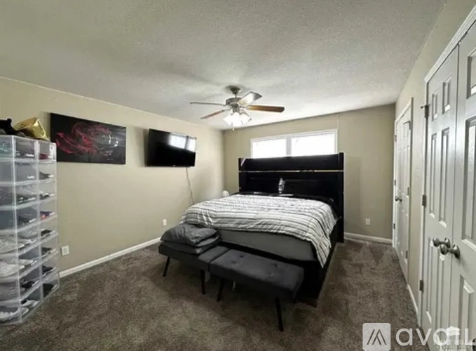 A bedroom with a bed, a ceiling fan, and a TV mounted on the wall.