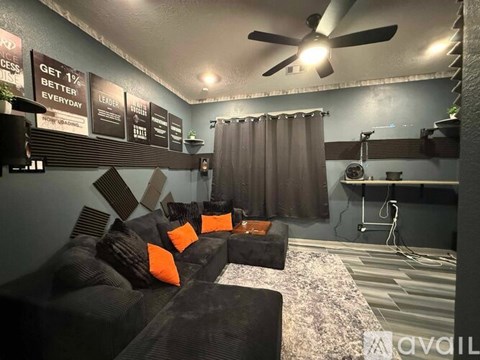 A living room with a black couch and a fan on the ceiling.