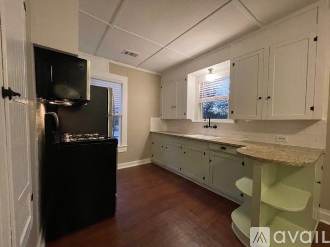A kitchen with a black fridge, white cabinets, and a wooden floor.