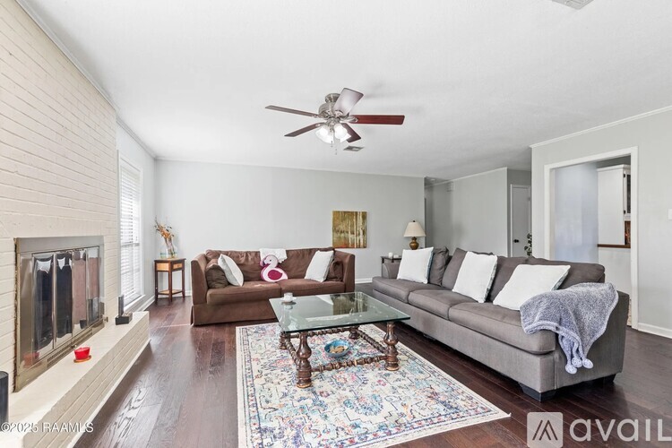 A living room with a brown couch, a glass table, and a ceiling fan.