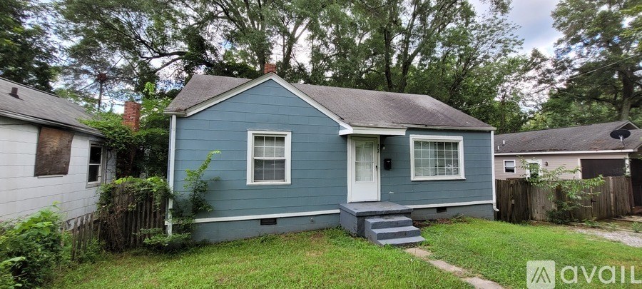 A blue house with a white door and a window is surrounded by a fence and greenery.