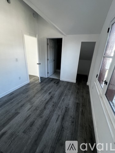 A room with wooden flooring and white walls, with a window on the right side.