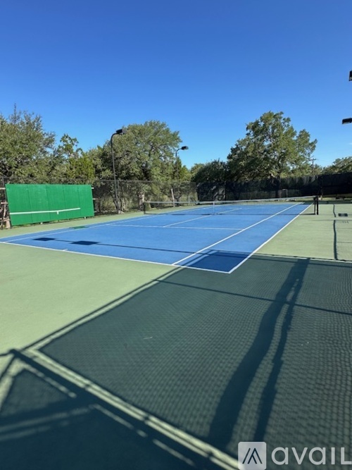 A tennis court with a green fence and trees in the background.