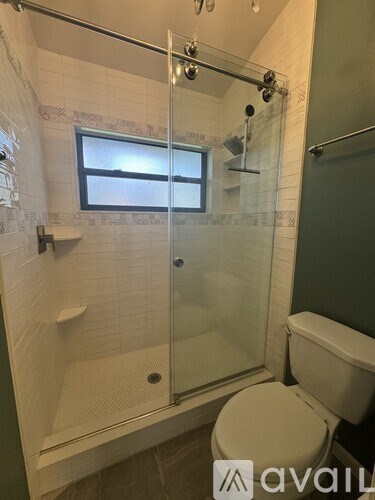 A bathroom with a toilet, a glass shower stall, and a window.
