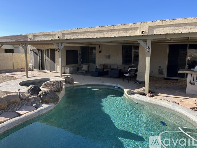 A pool in a backyard with a patio and a house in the background.
