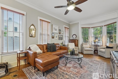 A living room with a brown leather sofa and a ceiling fan.