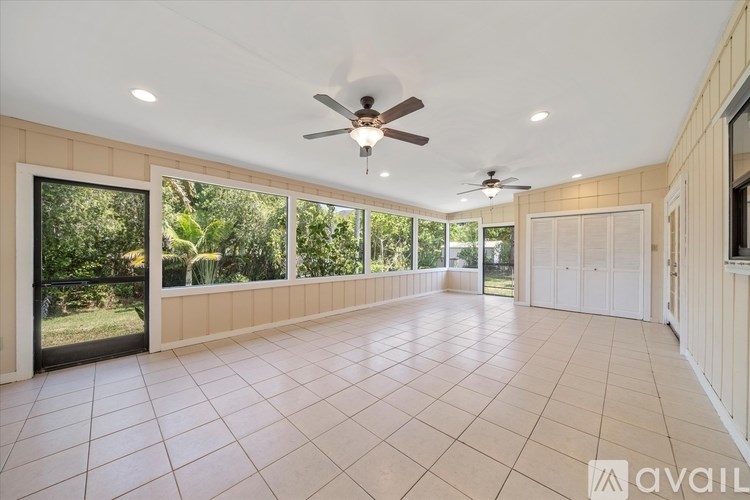 A spacious room with a ceiling fan and large windows overlooking a garden.