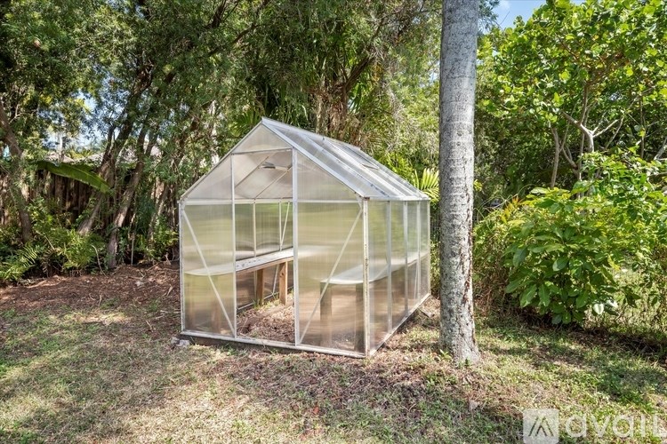 A greenhouse is situated in a grassy area with trees in the background.
