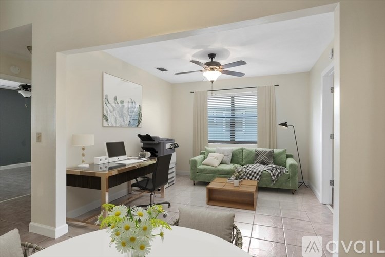 A living room with a couch, a table, a lamp, a fan, and a painting on the wall.