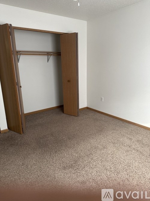 A room with a carpeted floor and a wooden wardrobe with a shelf.