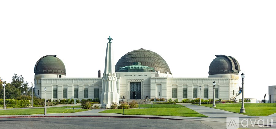 A large white building with three domes and a tall obelisk in front.