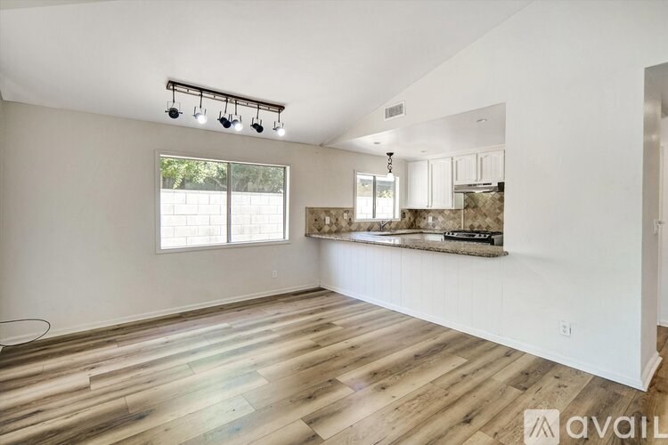 A spacious room with wooden floors and a kitchen area in the background.