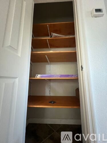 A white door is open to a pantry with a white wall and a small white box on the wall.