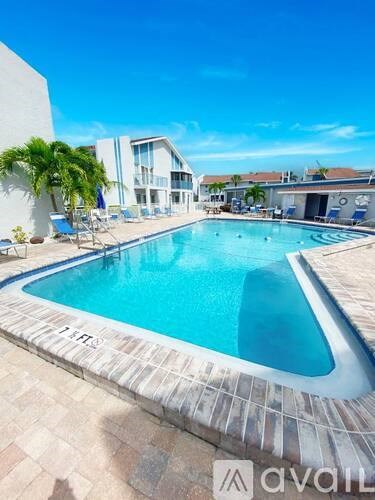 A large outdoor swimming pool surrounded by a tiled floor and lounge chairs.