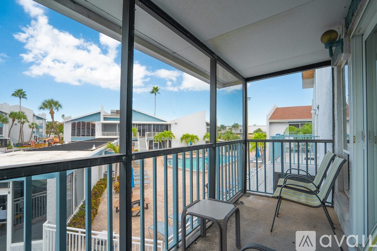 A balcony with a chair and table overlooking a pool and buildings.