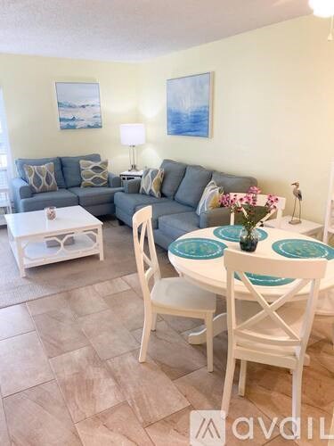 A living room with a grey couch, a white coffee table, and a white dining table with chairs.