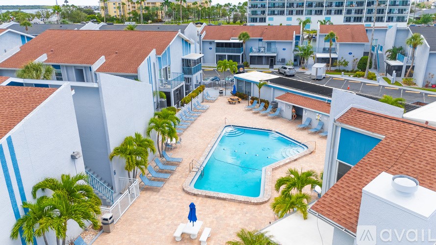 A pool surrounded by palm trees and a white building with a red roof.