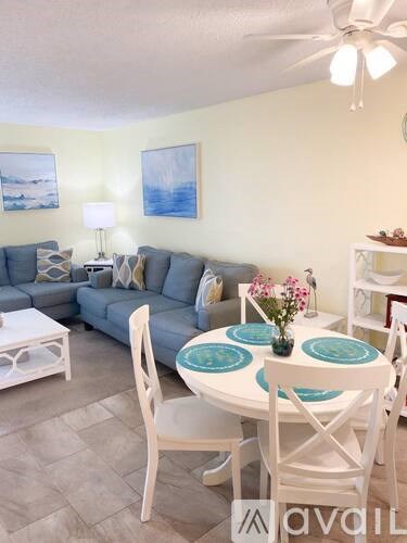 A living room with a grey couch, a white coffee table, a white dining table with blue plates and white chairs.