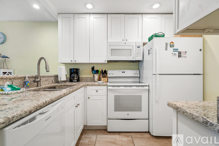 A kitchen with white cabinets and appliances, a sink, and a refrigerator.