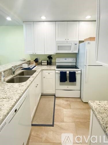 A kitchen with white cabinets and appliances, a sink, and a refrigerator.