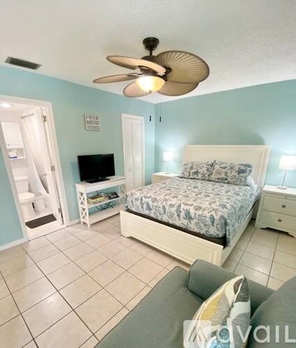 A bedroom with a bed, a television, and a ceiling fan.