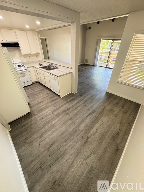 A room with wooden flooring and a mirror reflecting a kitchen.