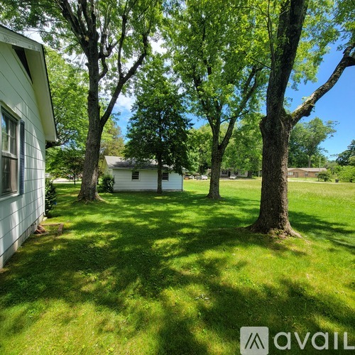 A white house is surrounded by trees in a sunny yard.