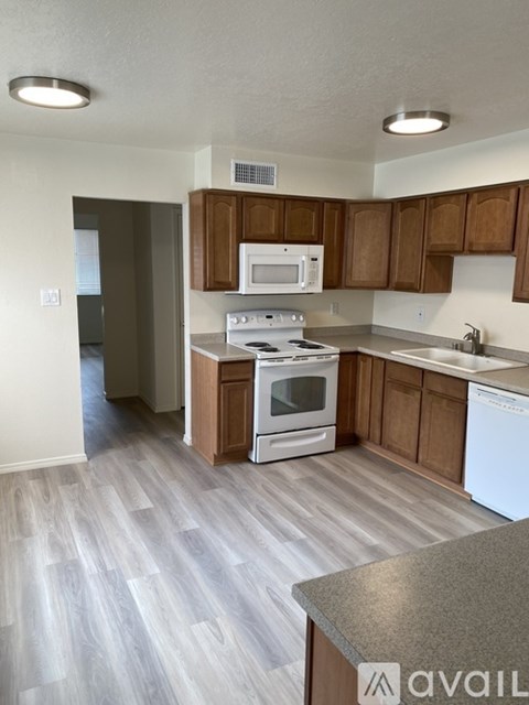 A kitchen with a white oven and microwave, brown cabinets, and a grey countertop.