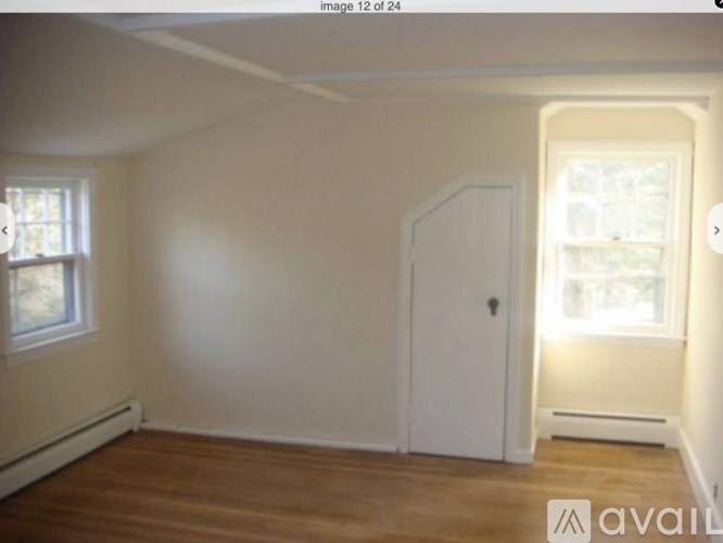 A room with a white door and a window with a view of trees.