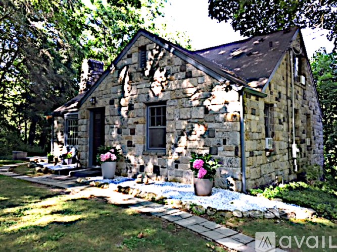 A stone house with a black door and windows is surrounded by a garden with pink flowers.