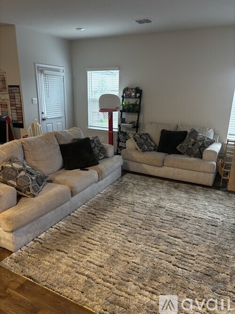 A living room with a large rug in the center and two couches with pillows.