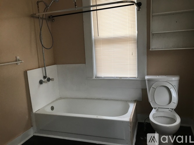 A white bathtub is in a bathroom with a toilet and a window.